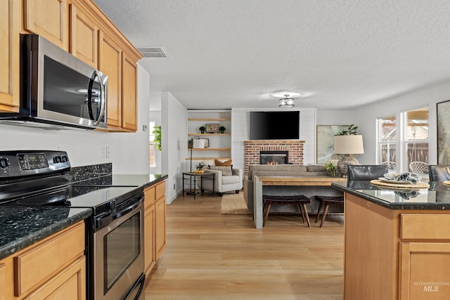 kitchen featuring a brick fireplace, visible vents, stainless steel appliances, a textured ceiling, and light wood-style floors