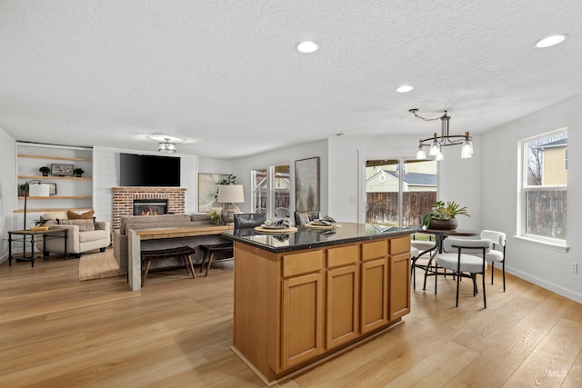 kitchen featuring decorative light fixtures, a center island, a textured ceiling, light wood-type flooring, and a brick fireplace