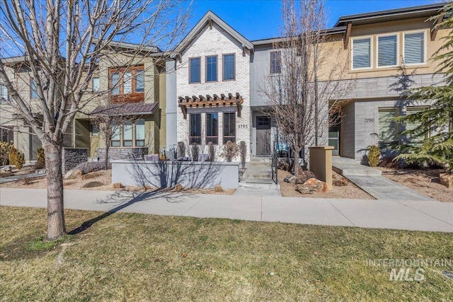 townhome / multi-family property featuring brick siding, a front lawn, and a pergola