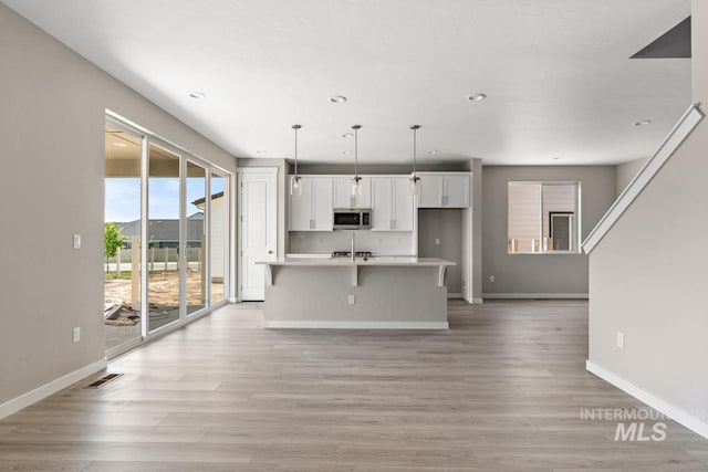 kitchen featuring stainless steel microwave, visible vents, an island with sink, light countertops, and white cabinetry