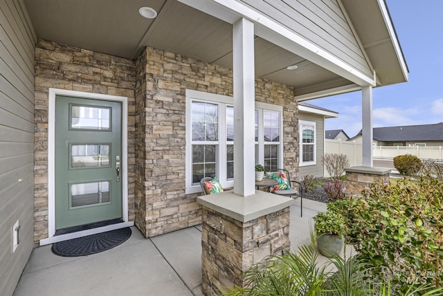 doorway to property with stone siding, fence, and covered porch