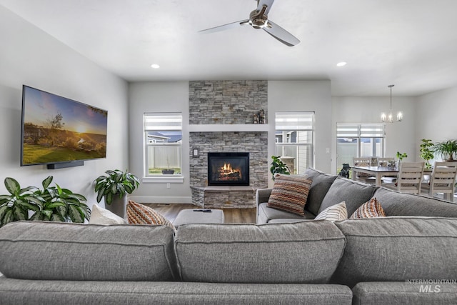 living area featuring a stone fireplace, ceiling fan with notable chandelier, wood finished floors, and a healthy amount of sunlight
