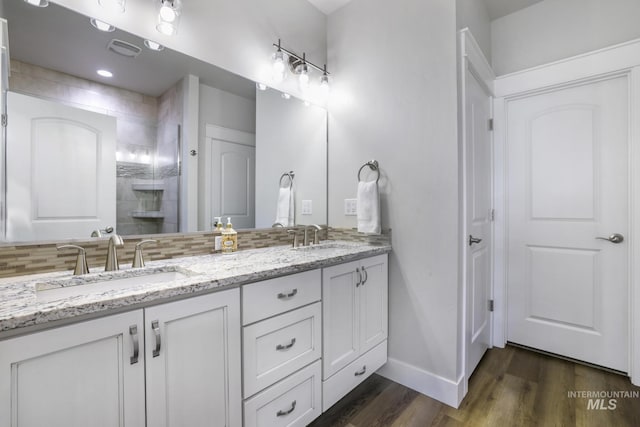 bathroom with a sink, backsplash, double vanity, and wood finished floors