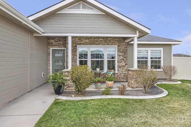 entrance to property with a porch, fence, stone siding, and a lawn
