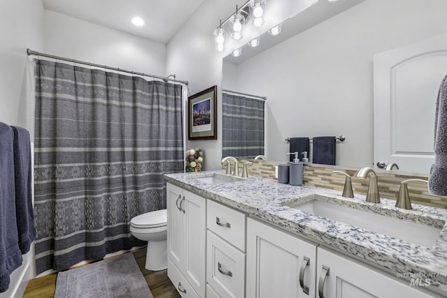 bathroom with toilet, wood finished floors, double vanity, and a sink