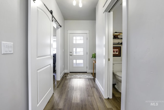doorway with a barn door, dark wood-style floors, and baseboards