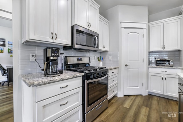 kitchen with white cabinets, appliances with stainless steel finishes, dark wood-style floors, light stone countertops, and backsplash