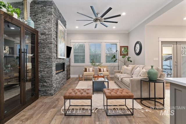 living room with a ceiling fan, wood finished floors, a fireplace, french doors, and crown molding