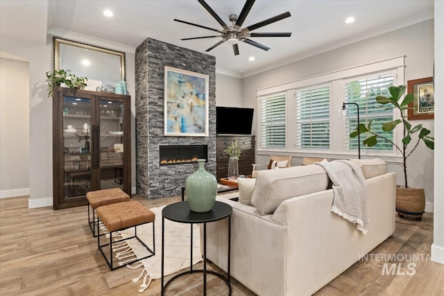 living room with crown molding, a ceiling fan, a fireplace, light wood-style flooring, and baseboards