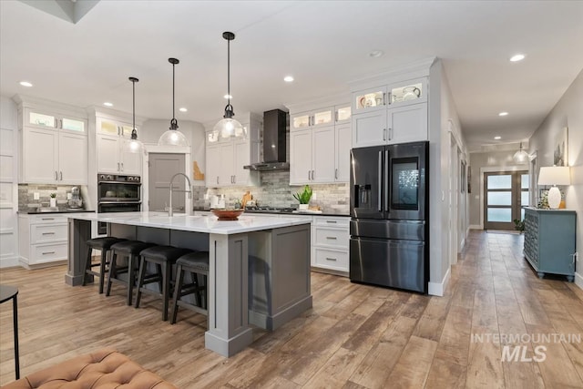 kitchen with stainless steel appliances, wall chimney range hood, backsplash, a breakfast bar, and white cabinetry