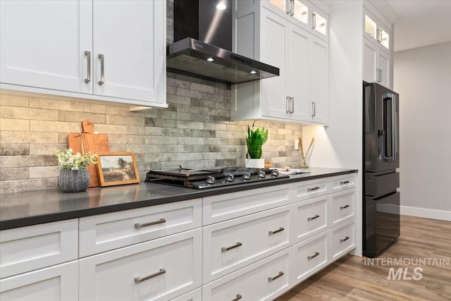 kitchen with wall chimney range hood, freestanding refrigerator, dark countertops, and wood finished floors