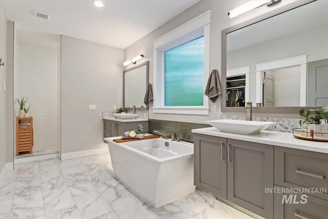 full bathroom featuring marble finish flooring, a freestanding bath, two vanities, baseboards, and recessed lighting