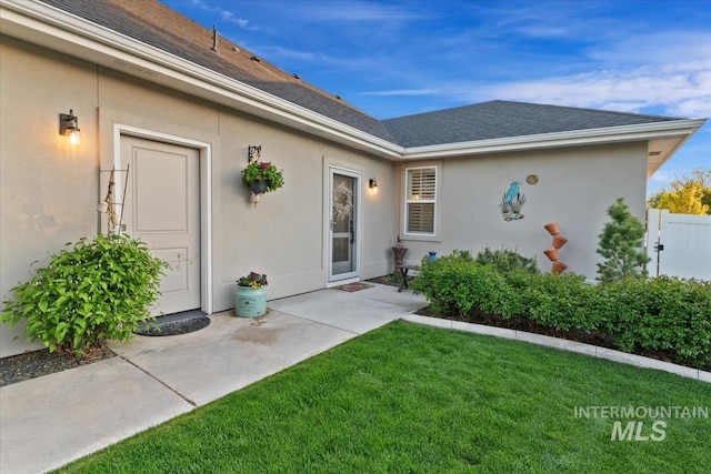 property entrance with a lawn, roof with shingles, and stucco siding