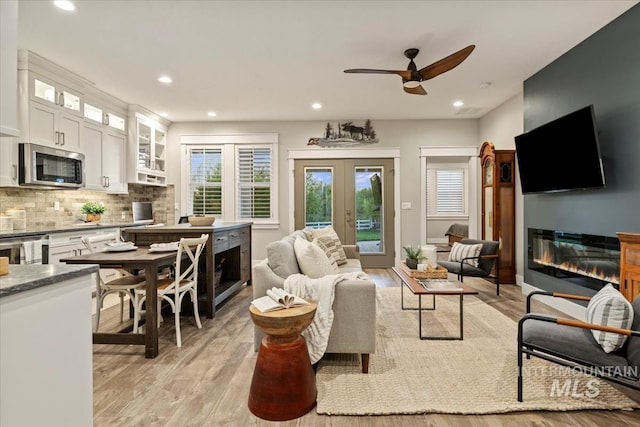 living room featuring a glass covered fireplace, light wood-type flooring, a ceiling fan, recessed lighting, and french doors
