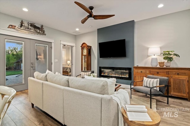 living area with light wood-type flooring, ceiling fan, recessed lighting, and a glass covered fireplace