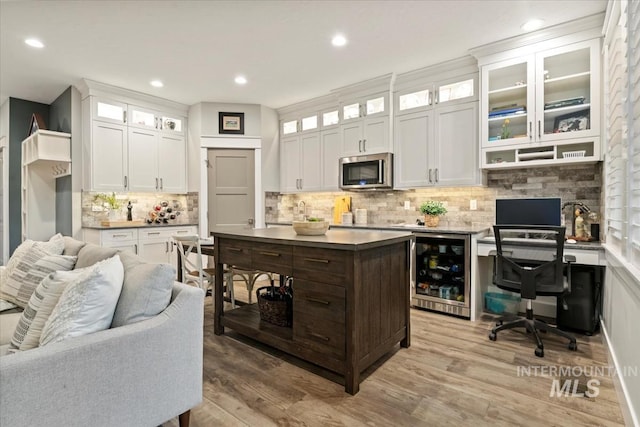 kitchen with beverage cooler, stainless steel microwave, backsplash, light wood-type flooring, and white cabinetry