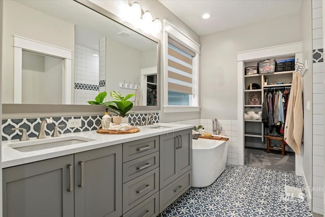full bath featuring tile walls, a soaking tub, a spacious closet, double vanity, and recessed lighting