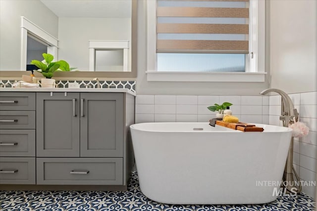 full bathroom featuring tile walls, vanity, a soaking tub, and wainscoting