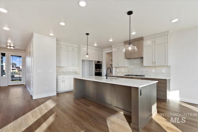 kitchen with white cabinetry, sink, backsplash, a center island with sink, and appliances with stainless steel finishes