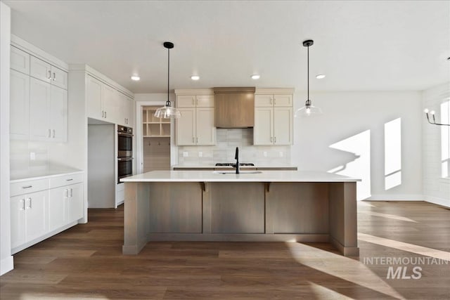 kitchen with stainless steel double oven, tasteful backsplash, dark hardwood / wood-style flooring, an island with sink, and pendant lighting