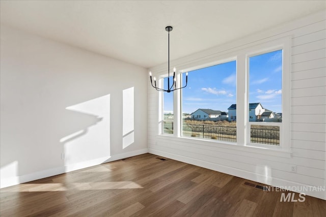 unfurnished dining area with hardwood / wood-style flooring, a notable chandelier, and wood walls