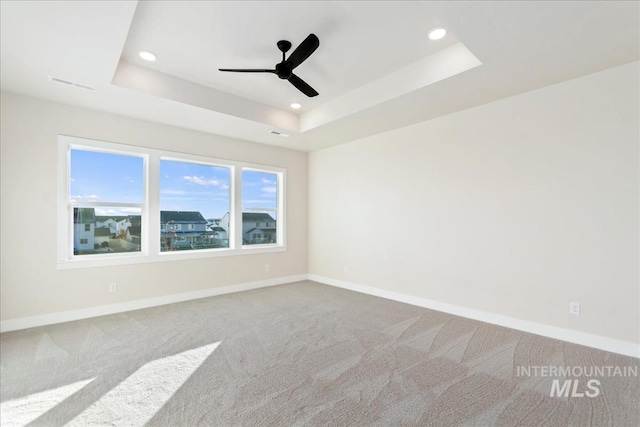 empty room featuring ceiling fan, a raised ceiling, and carpet floors