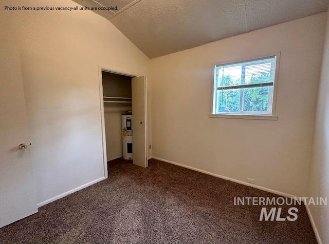 unfurnished bedroom with a textured ceiling, a closet, lofted ceiling, and dark colored carpet