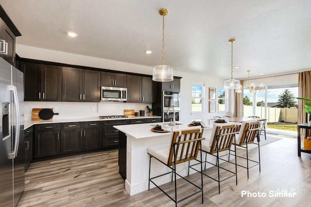 kitchen with stainless steel appliances, a sink, a kitchen bar, light wood-style floors, and light countertops