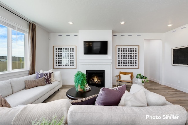 living room featuring baseboards, wood finished floors, a glass covered fireplace, and recessed lighting
