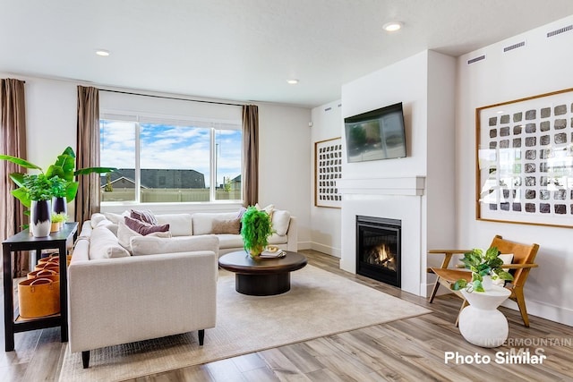 living room with baseboards, a glass covered fireplace, wood finished floors, and recessed lighting