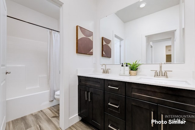 bathroom with wood finished floors, a sink, double vanity, and toilet