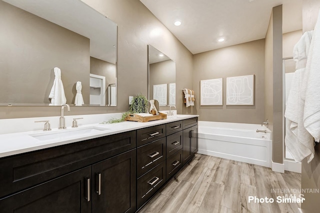 full bathroom with double vanity, wood finished floors, a garden tub, and a sink