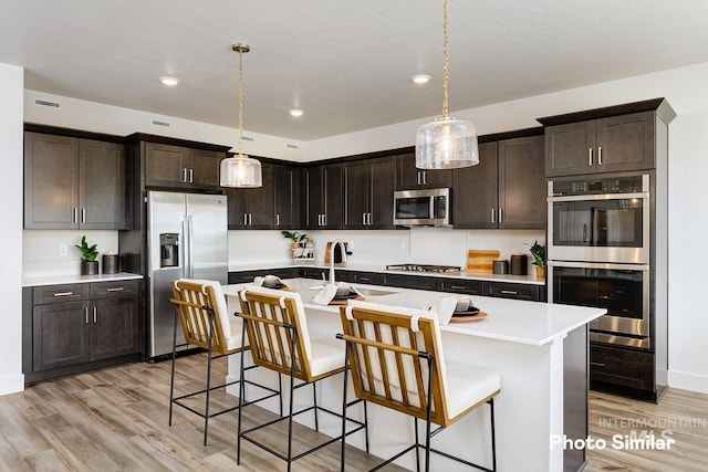 kitchen with light wood finished floors, dark brown cabinetry, stainless steel appliances, and a sink