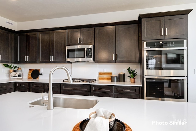 kitchen featuring dark brown cabinetry, stainless steel appliances, light countertops, and a sink