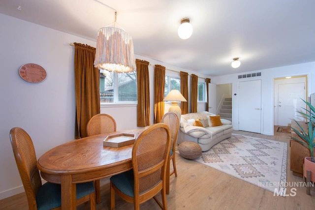 dining area with light wood-type flooring, stairs, visible vents, and a chandelier