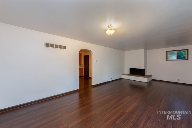 unfurnished living room with arched walkways, dark wood finished floors, visible vents, and baseboards