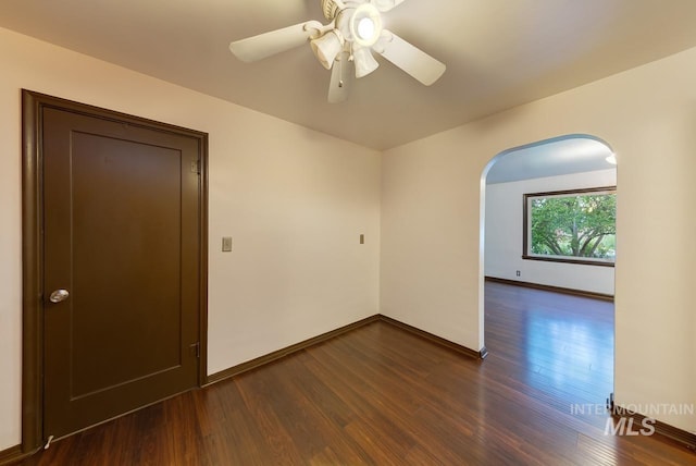 empty room with a ceiling fan, arched walkways, dark wood-style flooring, and baseboards