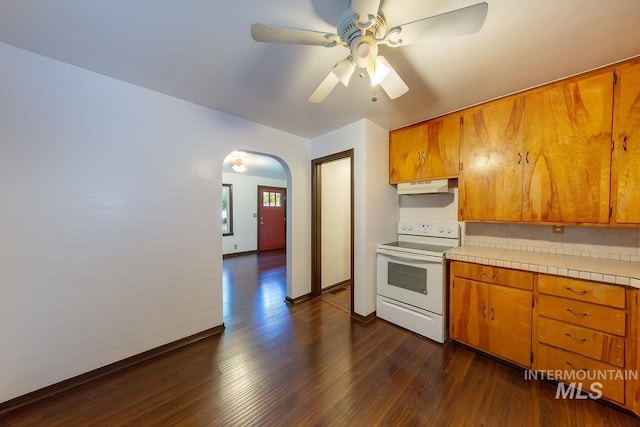 kitchen featuring arched walkways, tile countertops, under cabinet range hood, dark wood-style flooring, and white electric range oven