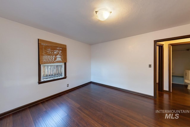 spare room featuring dark wood-style floors and baseboards