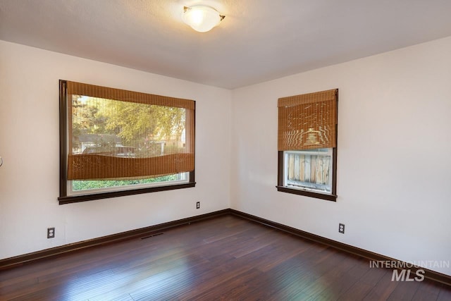 spare room featuring dark wood-type flooring, visible vents, and baseboards