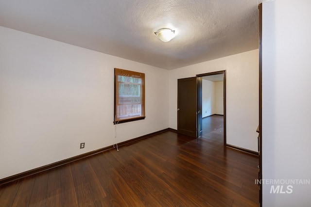 spare room with dark wood-style flooring, a textured ceiling, and baseboards