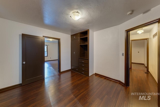 unfurnished bedroom featuring baseboards, a textured ceiling, visible vents, and dark wood-type flooring