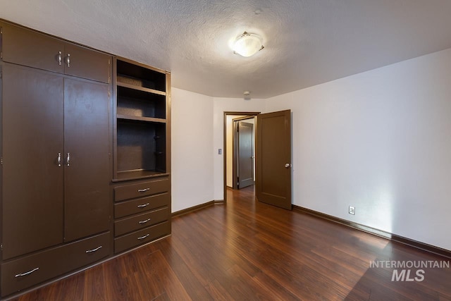 unfurnished bedroom with dark wood-style floors, a textured ceiling, a closet, and baseboards