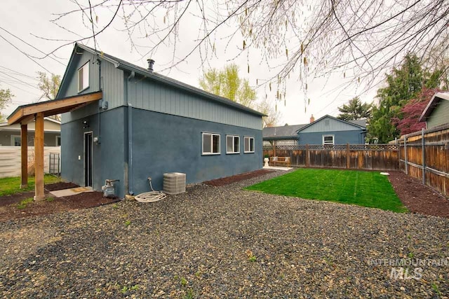 back of property featuring a fenced backyard, a lawn, central AC, and stucco siding