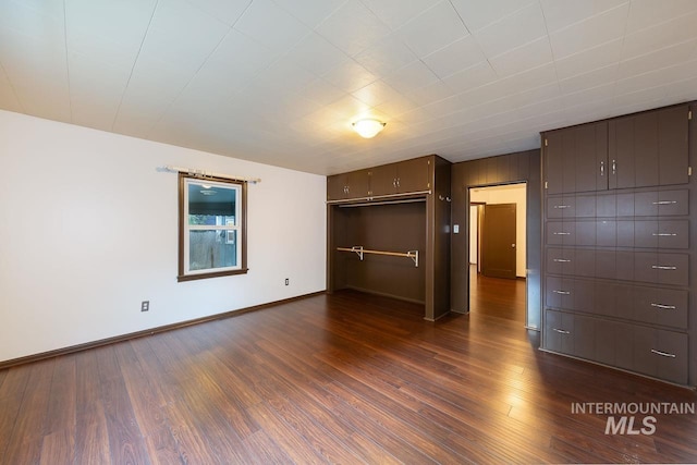 unfurnished bedroom with dark wood-style flooring, a closet, and baseboards