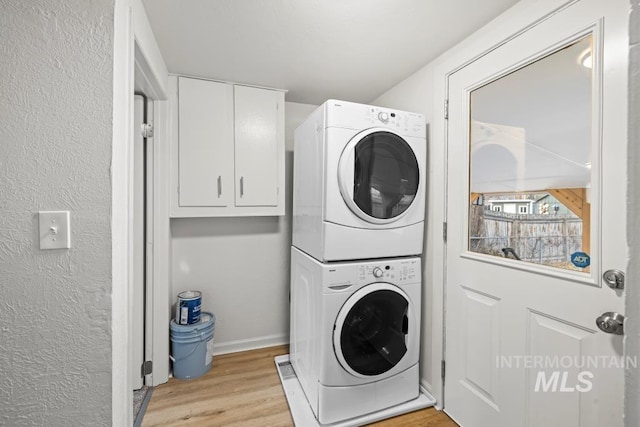 clothes washing area with stacked washer / dryer, light wood-type flooring, and cabinets