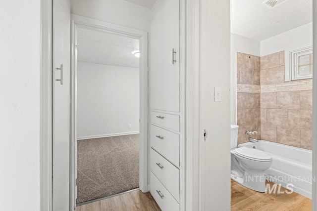 bathroom with toilet, a textured ceiling, tiled shower / bath combo, and hardwood / wood-style flooring