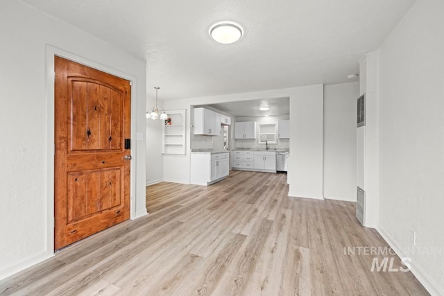 unfurnished living room with light wood-type flooring, built in features, a notable chandelier, and sink