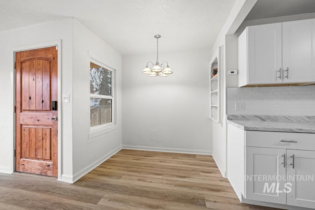 kitchen featuring white cabinets, decorative light fixtures, light hardwood / wood-style floors, backsplash, and a chandelier