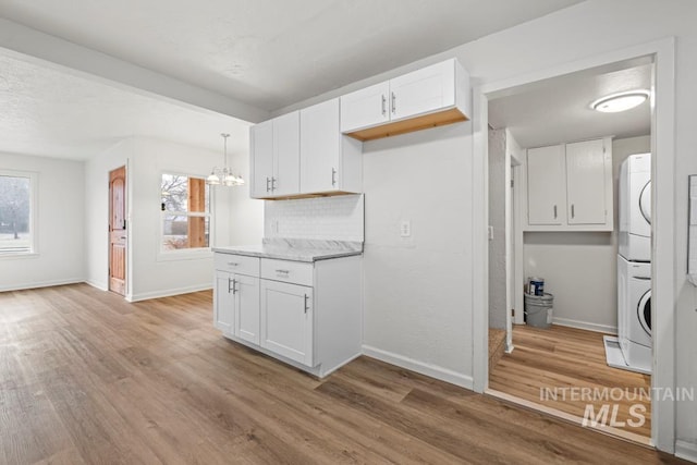 kitchen with a healthy amount of sunlight, stacked washer and clothes dryer, and white cabinetry